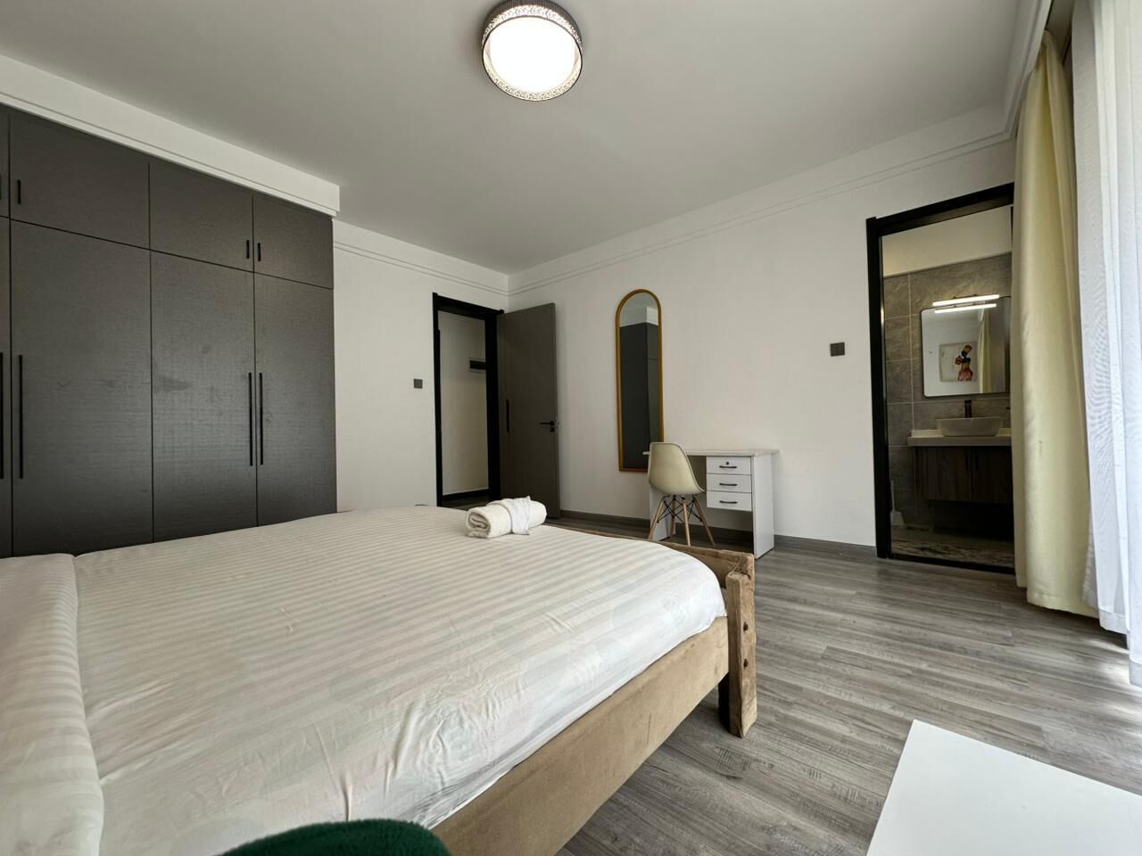 A modern hotel room with a large bed, a desk, a mirror, and a wardrobe.