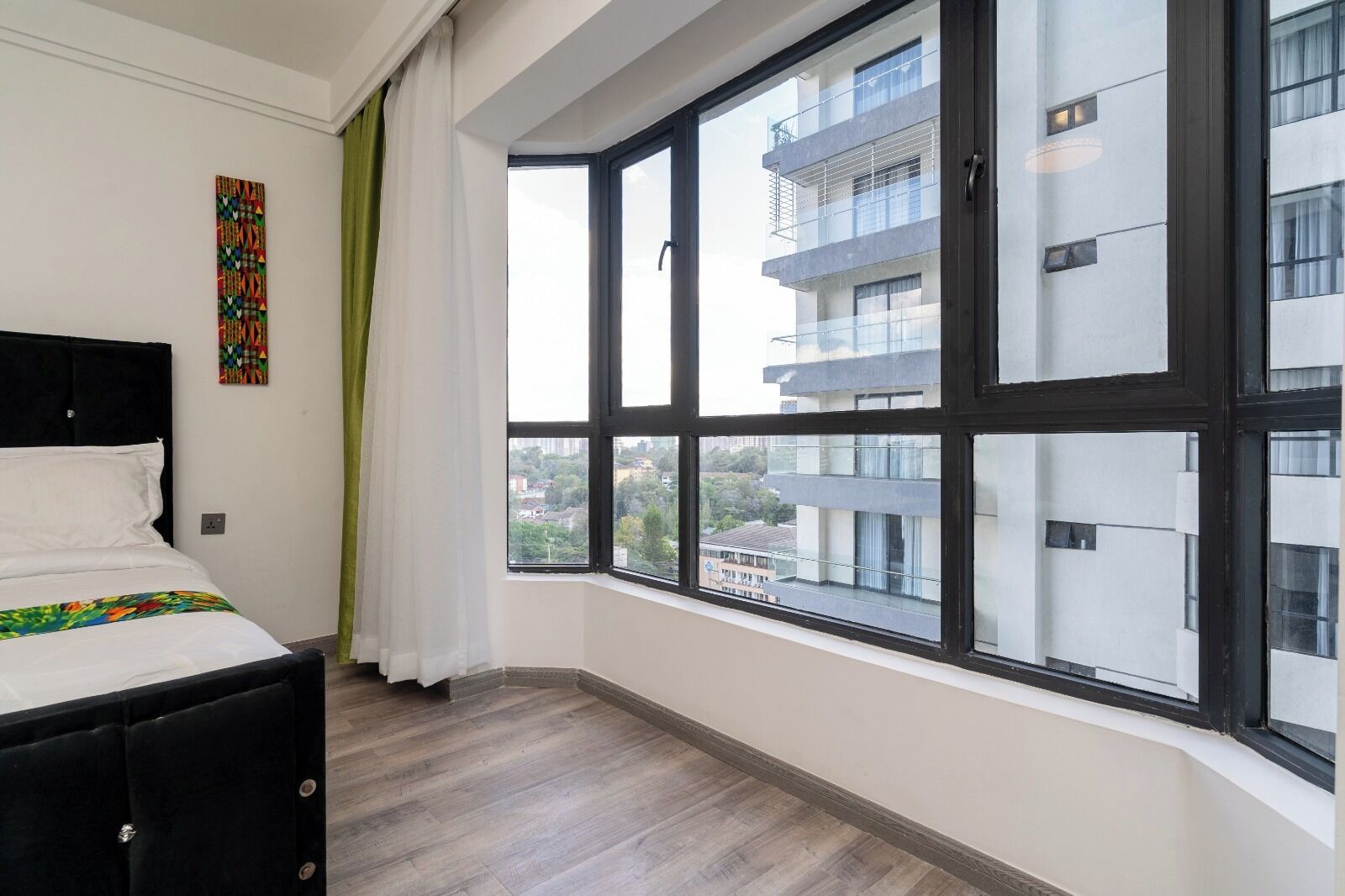Une chambre avec une grande fenêtre, un lit et une vue sur un bâtiment à l’extérieur.