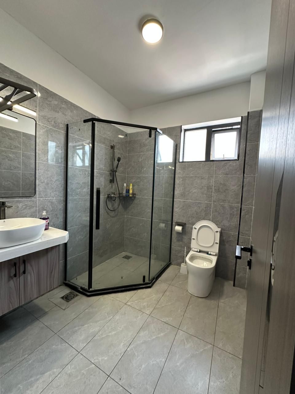 Een moderne badkamer met een glazen douchecabine, toilet en een wastafel met spiegel.