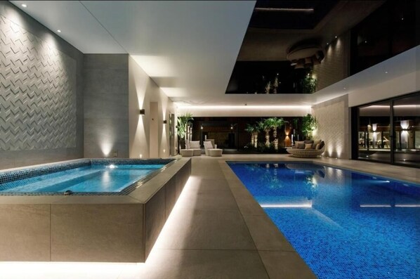 Ein moderner Poolbereich im Innenbereich mit zwei Pools, Liegebereichen und stimmungsvoller Beleuchtung.