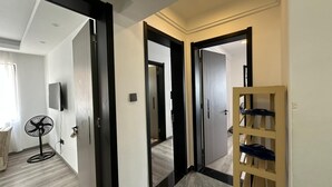 Un pasillo con piso de madera, una puerta con marco negro, un espejo y un ventilador.