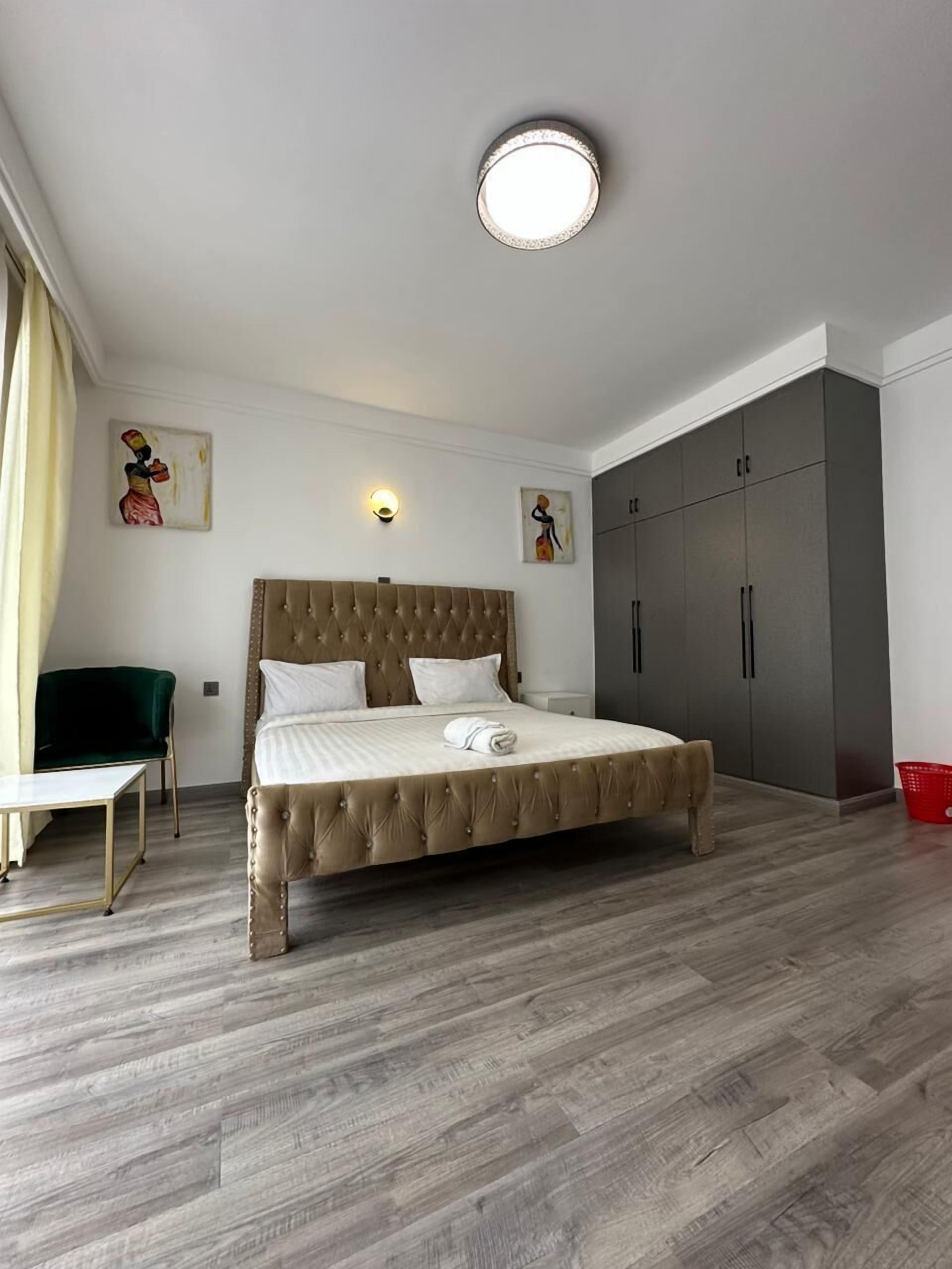 Een slaapkamer met een groot bed, een groene fauteuil, een kledingkast en twee wandlampen.