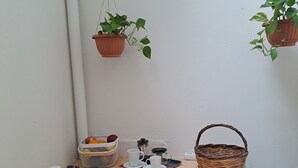 Eine kleine, gemütliche Küchenzeile mit einer Holzausziehtischplatte, Obstkorb, Kaffeemaschine und hängenden Topfpflanzen.