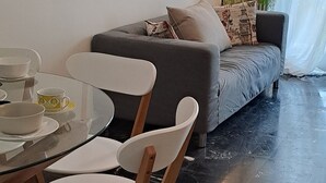 Un soggiorno moderno con un divano grigio, un tavolo da pranzo in vetro e sedie bianche, e una lampada da terra.