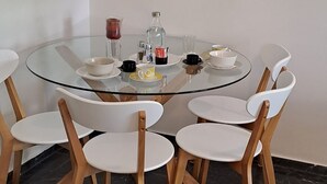 Zona pranzo con tavolo in vetro circondato da sedie bianche, pavimento in marmo nero e due dipinti astratti alle pareti.