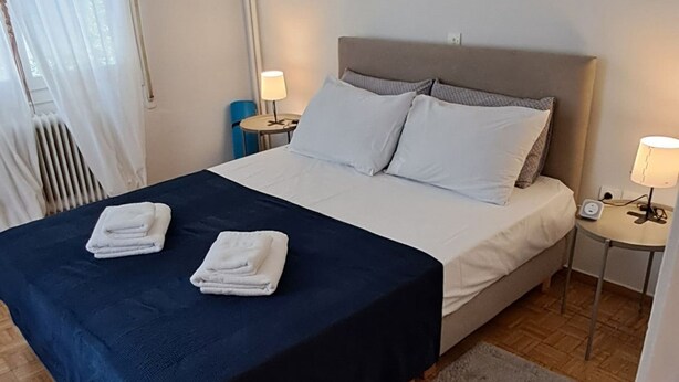 Un letto rifatto con una coperta blu scuro e cuscini bianchi, un comodino con una lampada e un pavimento in parquet di legno.