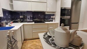 Ett modernt kök med vita skåp, en svart bänkskiva och en kakelvägg som föreställer en stadsbild.