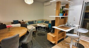 Ein modernes Wohnzimmer mit einer Couch, einem Esstisch und einer Küchenzeile mit Arbeitsplatte und Regalen.