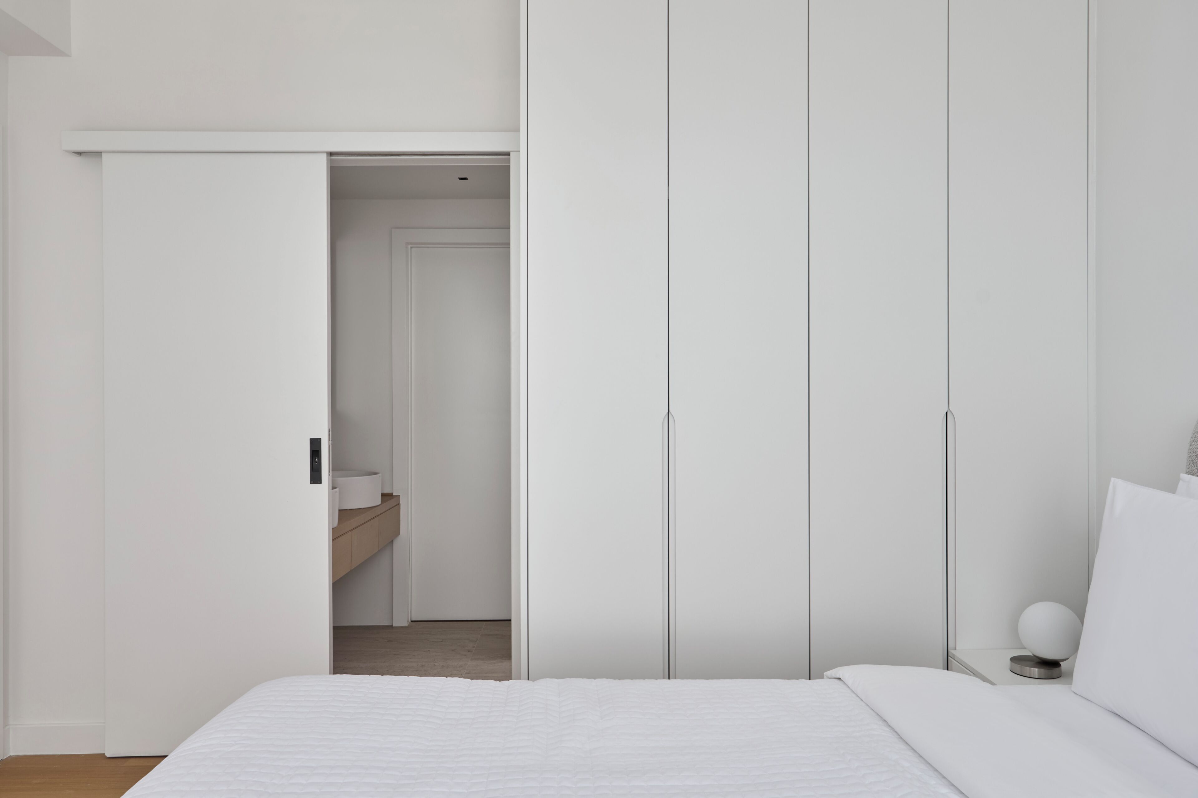 A bedroom with a bed, white wardrobe, and a small bedside table with a lamp.