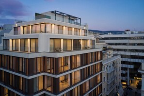 Un hôtel à plusieurs étages au design moderne, doté de balcons, de grandes fenêtres et d’une terrasse sur le toit.