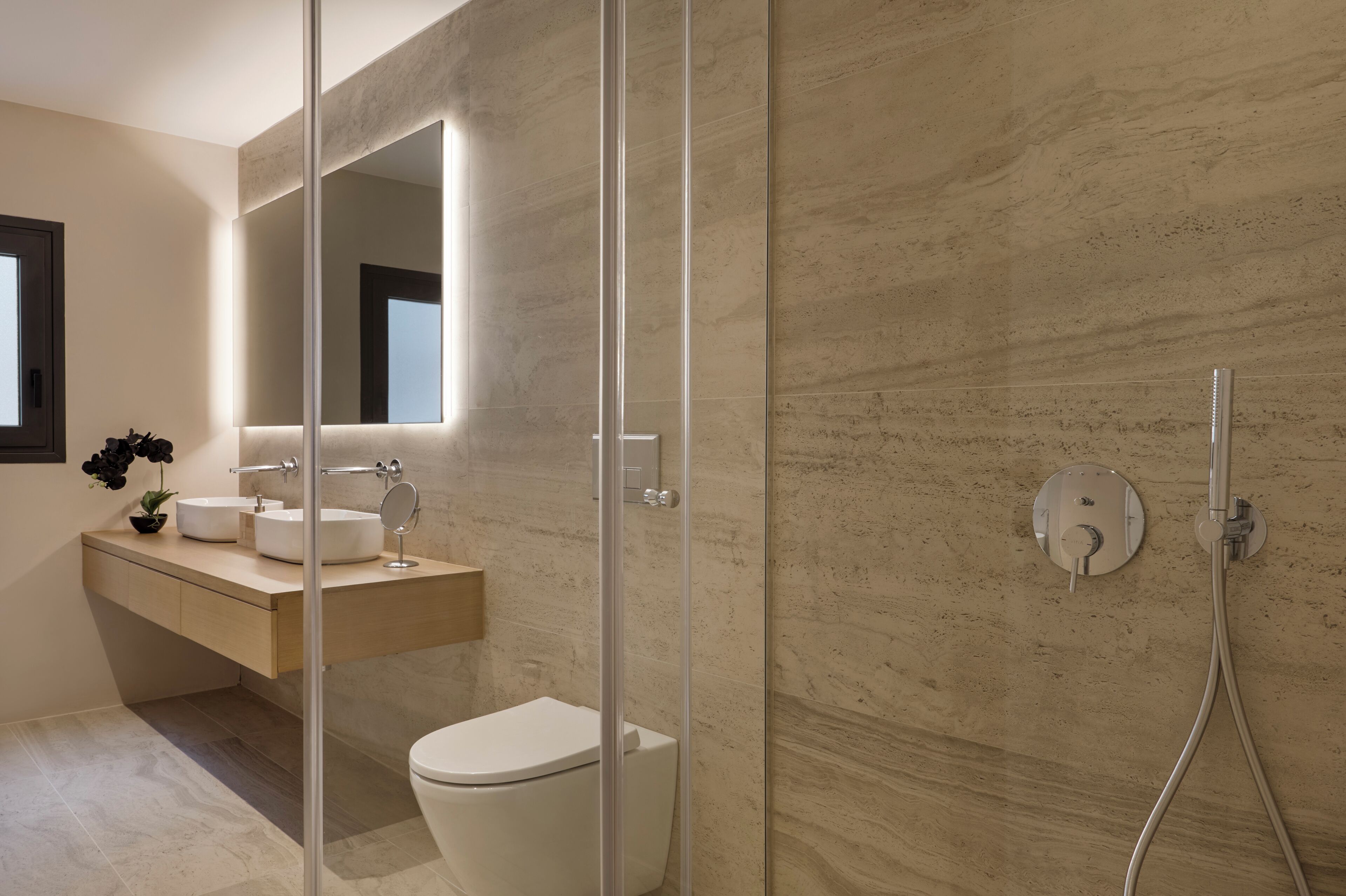 A modern bathroom with a glass-enclosed shower, a white toilet, and a vanity with a mirror and two sinks.