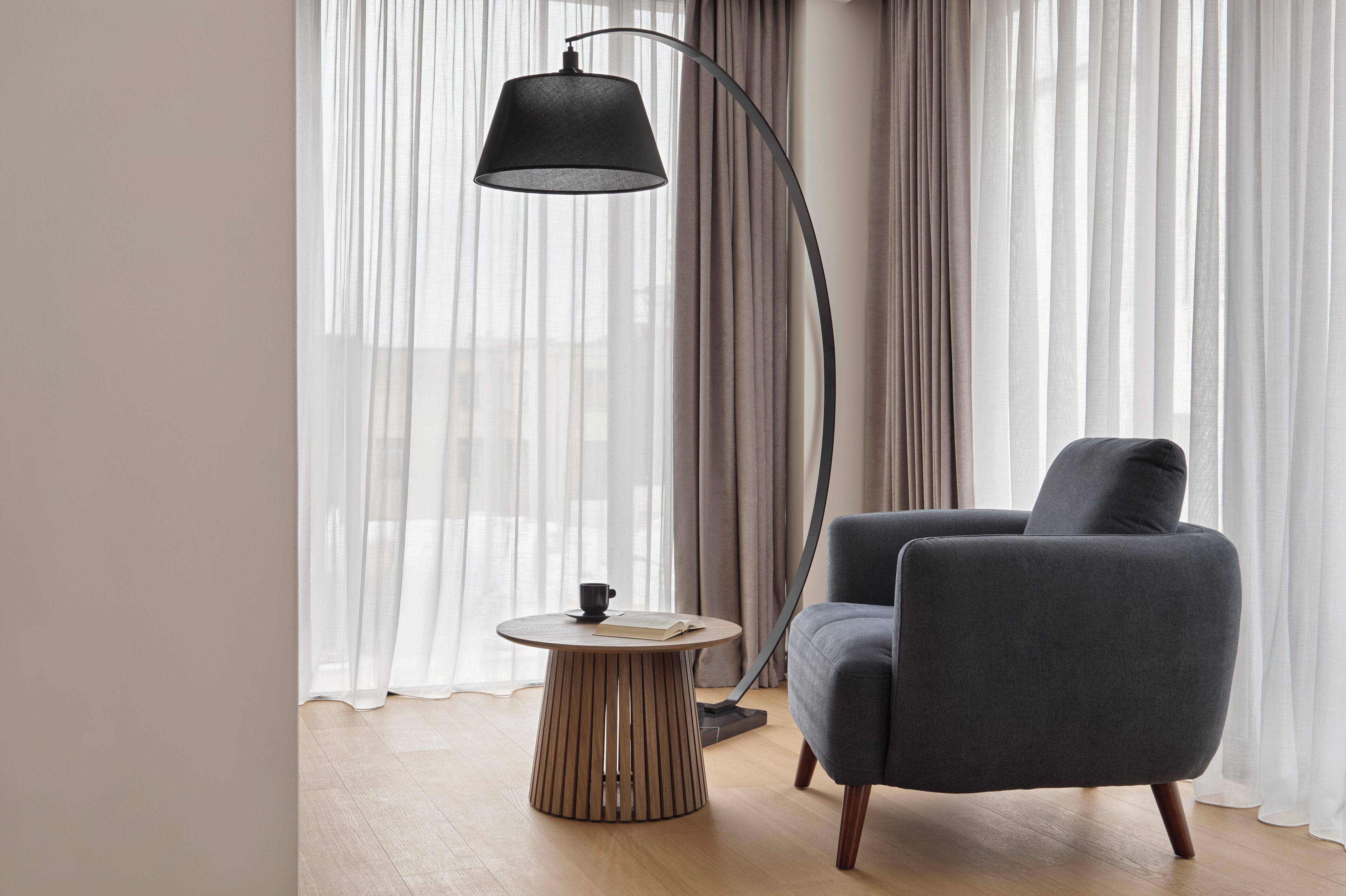 A modern living room with a round wooden side table, a dark grey armchair, and a floor lamp.