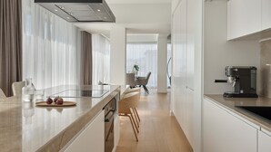 A modern kitchen with a central island, a coffee machine, and a dining area with chairs and a table. - September Athens Residences (Athens)