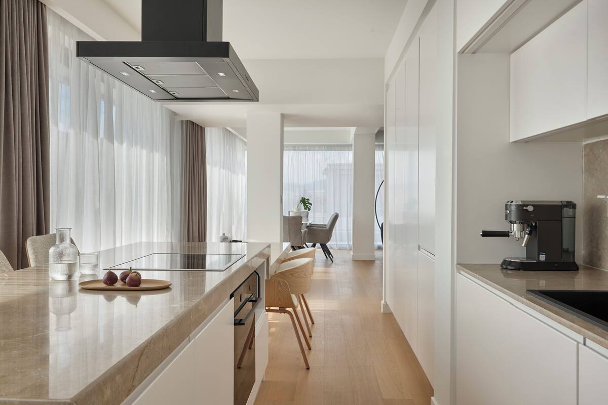 A modern kitchen with a central island, a coffee machine, and a dining area with chairs and a table.