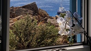 A window with a clear view of rocky terrain and a ship in the distance. - Smart  4 pers. apar. in Costa Ilios resort Myconos (Mikonos)