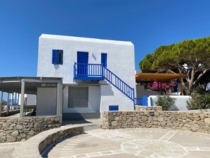 A white building with blue accents, a stone wall, and a covered outdoor area. - Smart  4 pers. apar. in Costa Ilios resort Myconos (Mikonos)