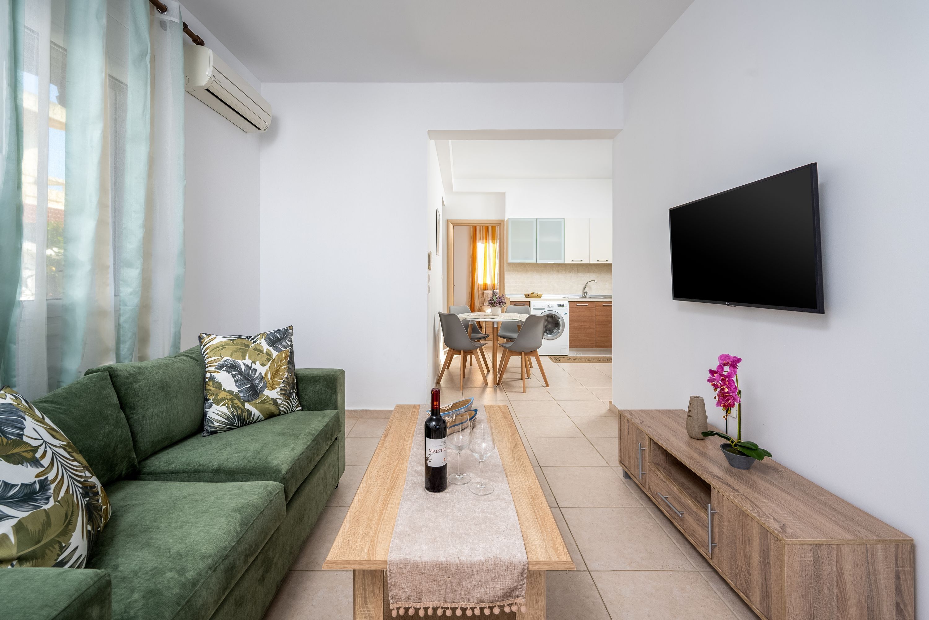 A modern living room with a green sofa, a wooden coffee table, and a flat-screen TV mounted on the wall.