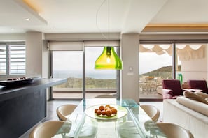 Ein moderner Essbereich mit einem Glastisch, Stühlen und einer Schale Orangen. Ein großes Fenster bietet Blick auf die Landschaft.