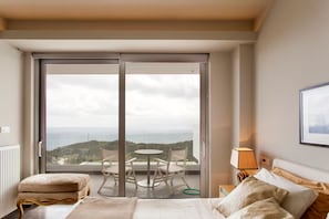 Ein Hotelzimmer mit Bett, kleinem Tisch mit Stühlen, Meerblick und einem Balkon mit Tisch und Stühlen.