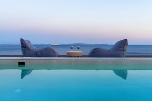 A poolside view with two lounge chairs and a small ottoman, overlooking a calm sea and distant islands.