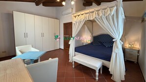 Ein Schlafzimmer mit Himmelbett, einem weißen Kleiderschrank, einem kleinen Nachttisch und einer Bank.