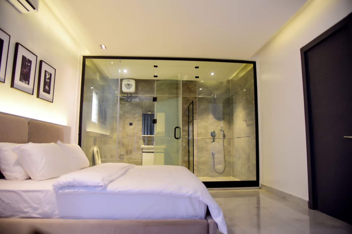 Ein modernes Hotelzimmer mit einem großen Bett, einer gläsernen Duschkabine und gerahmten Bildern an der Wand.
