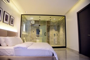 Ein modernes Hotelzimmer mit einem großen Bett, einer gläsernen Duschkabine und gerahmten Bildern an der Wand.