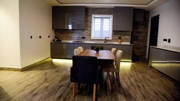 A modern kitchen with a dining area, featuring a wooden floor, dark cabinets, and a window providing natural light.