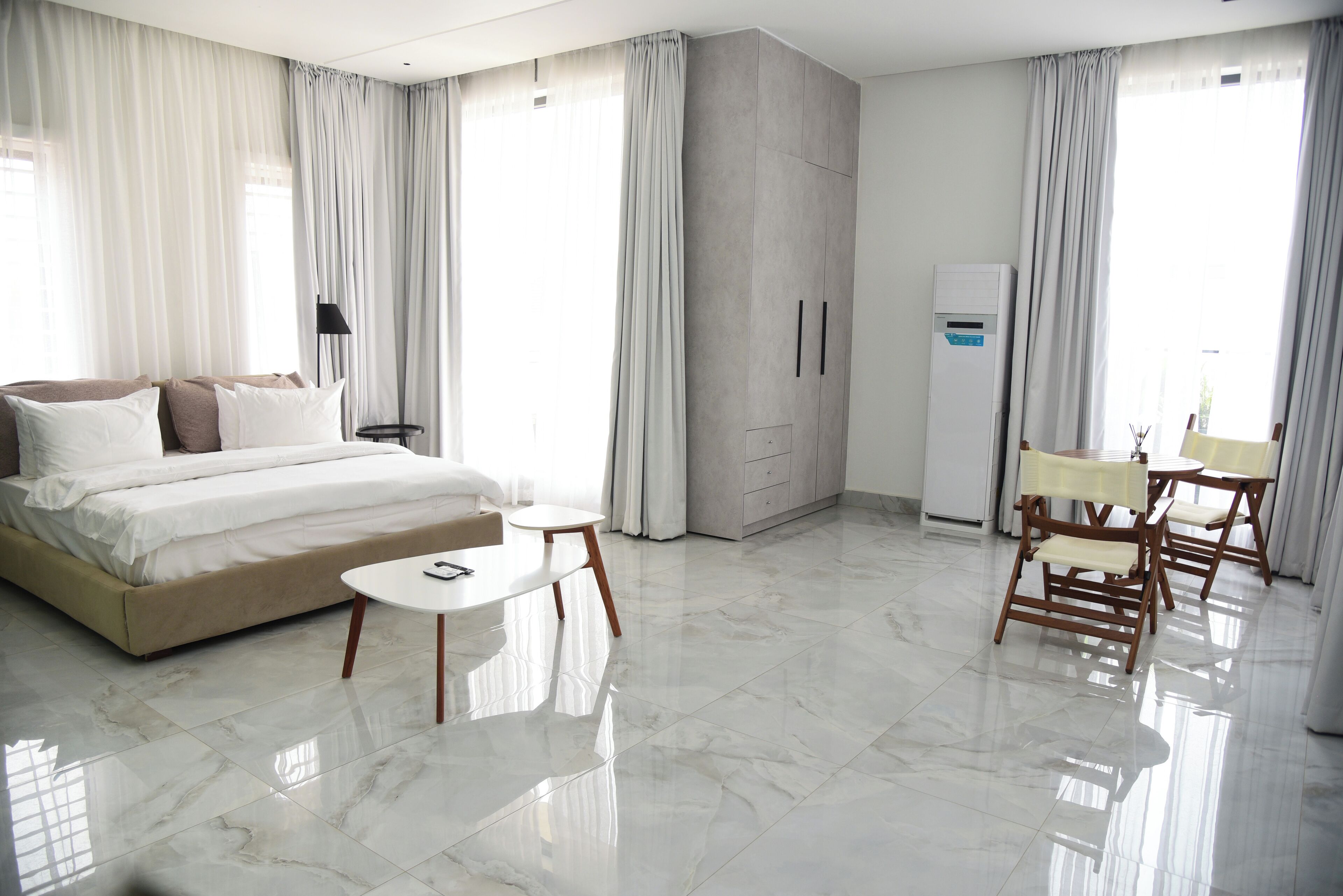 Una habitación de hotel moderna con una cama grande, una mesita redonda pequeña, un espacio de descanso con sillas y un equipo de aire acondicionado integrado.