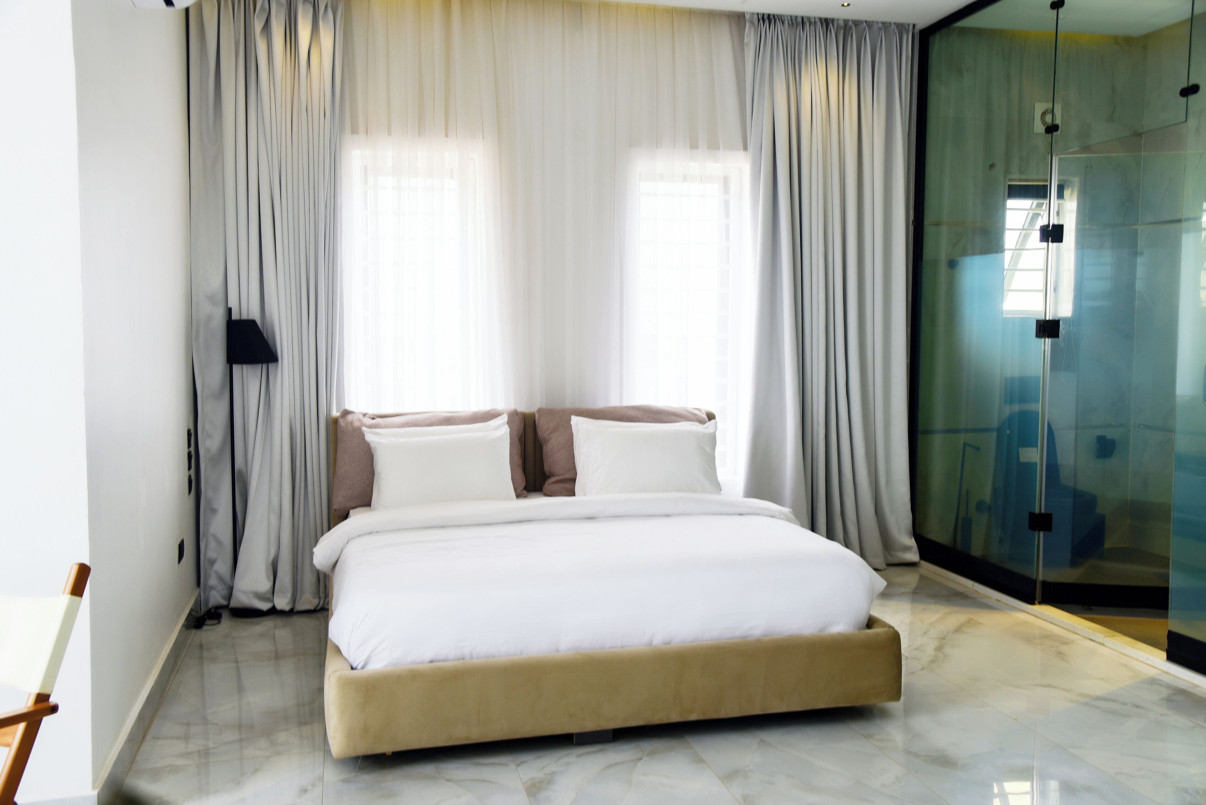 A modern bedroom with a large bed, white bedding, and sheer curtains.
