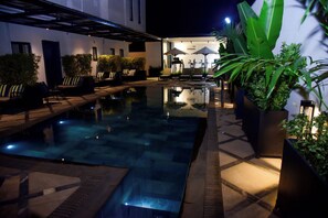 A nighttime swimming pool area with lounge chairs, umbrellas, and potted plants. - Hotel De Alommah Kubwa Abuja Nigeria (Abuja)