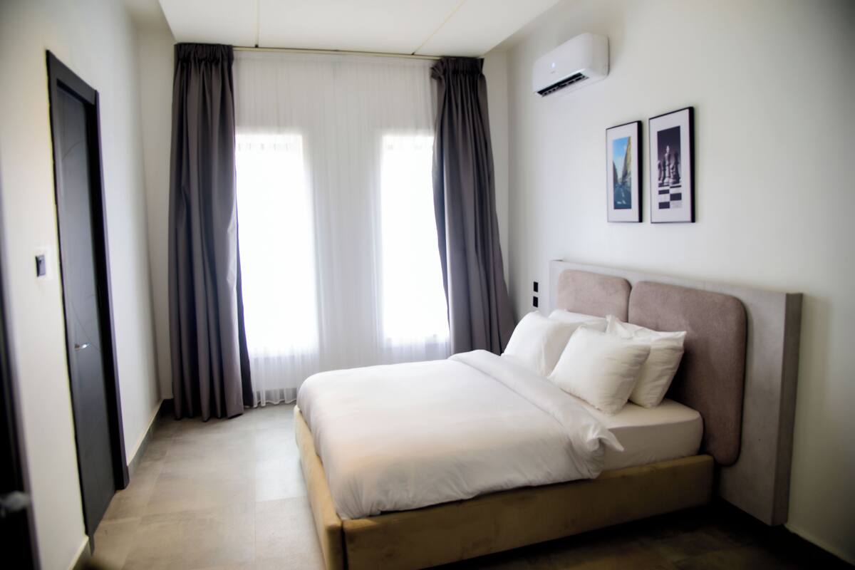 Ein Schlafzimmer mit einem Bett, Vorhängen, einer Wandklimaanlage und zwei gerahmten Bildern.