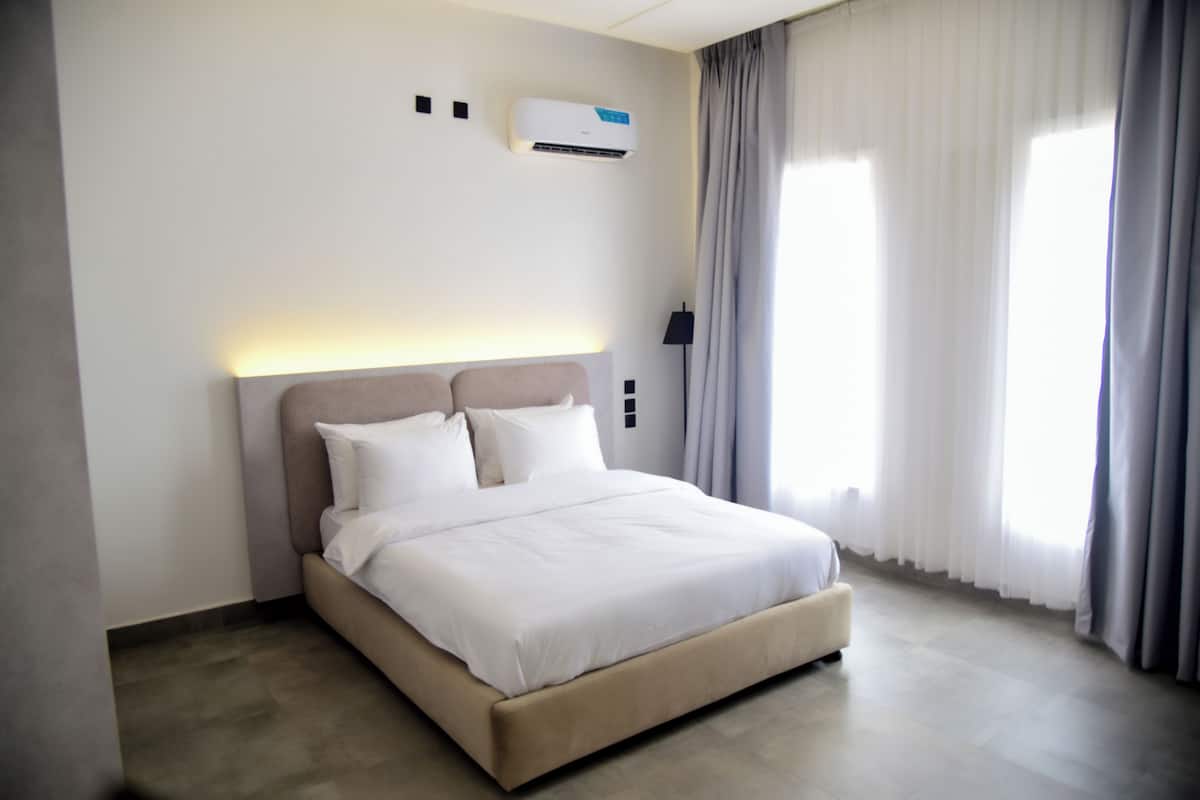 Ein modernes Hotelzimmer mit einem großen Bett, einer Wandklimaanlage und einem mit Vorhängen versehenen Fenster.