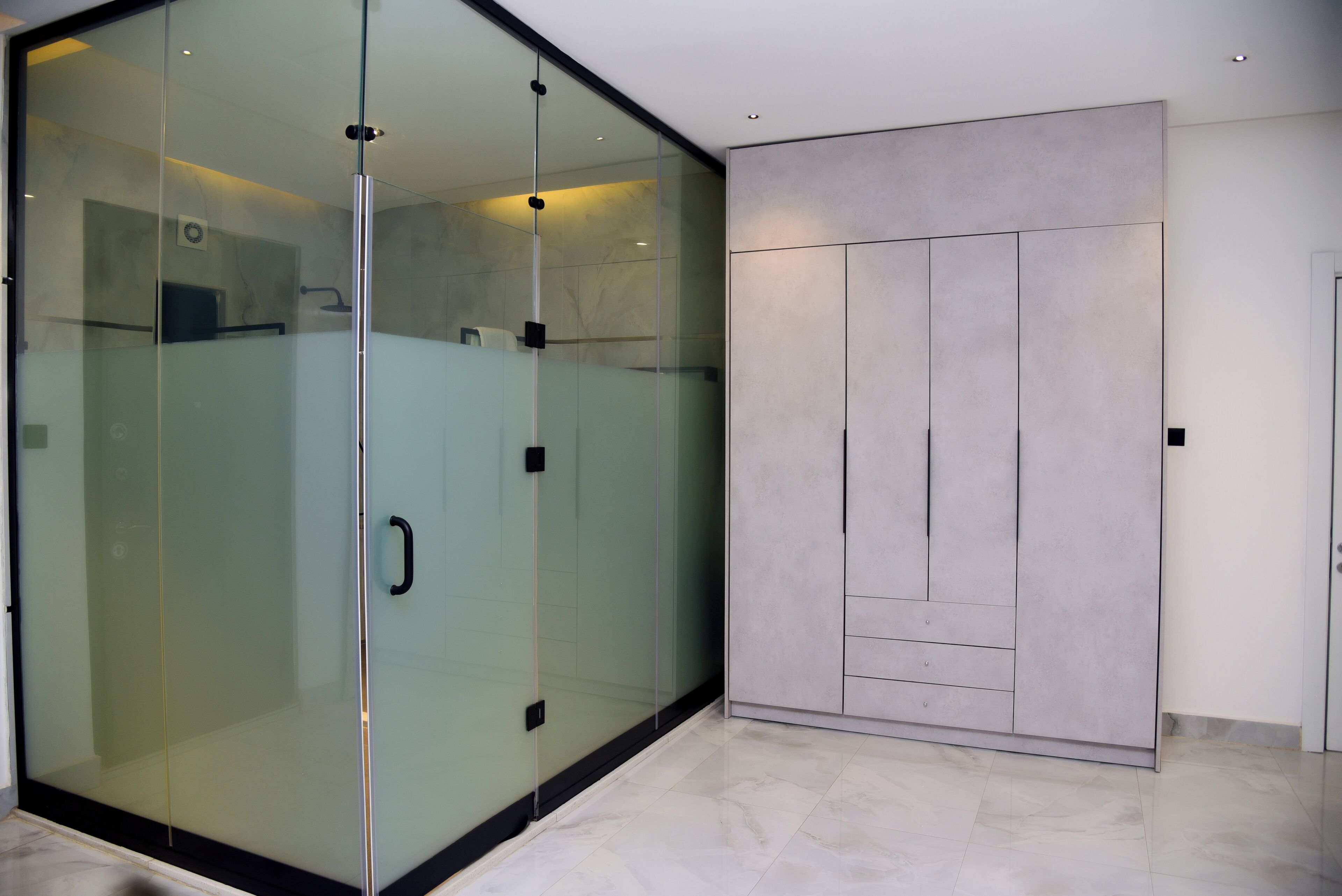 A modern room with a glass partition, a grey wardrobe, and a tiled floor.
