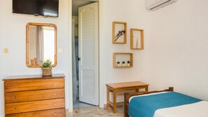 Een slaapkamer met een houten dressoir, een bed met een blauwe spreideken, een kleine tafel en een aan de muur bevestigde televisie.