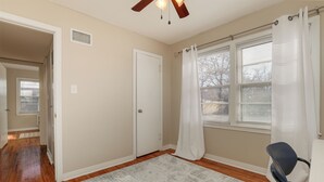 A room with hardwood flooring, a white door, a ceiling fan, and a window with white curtains. - Charming 3-bedroom house in quiet neighborhood (Wichita)