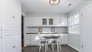 A kitchen with white cabinets, a dining table with chairs, and a window with blinds. - Charming 3-bedroom house in quiet neighborhood (Wichita)
