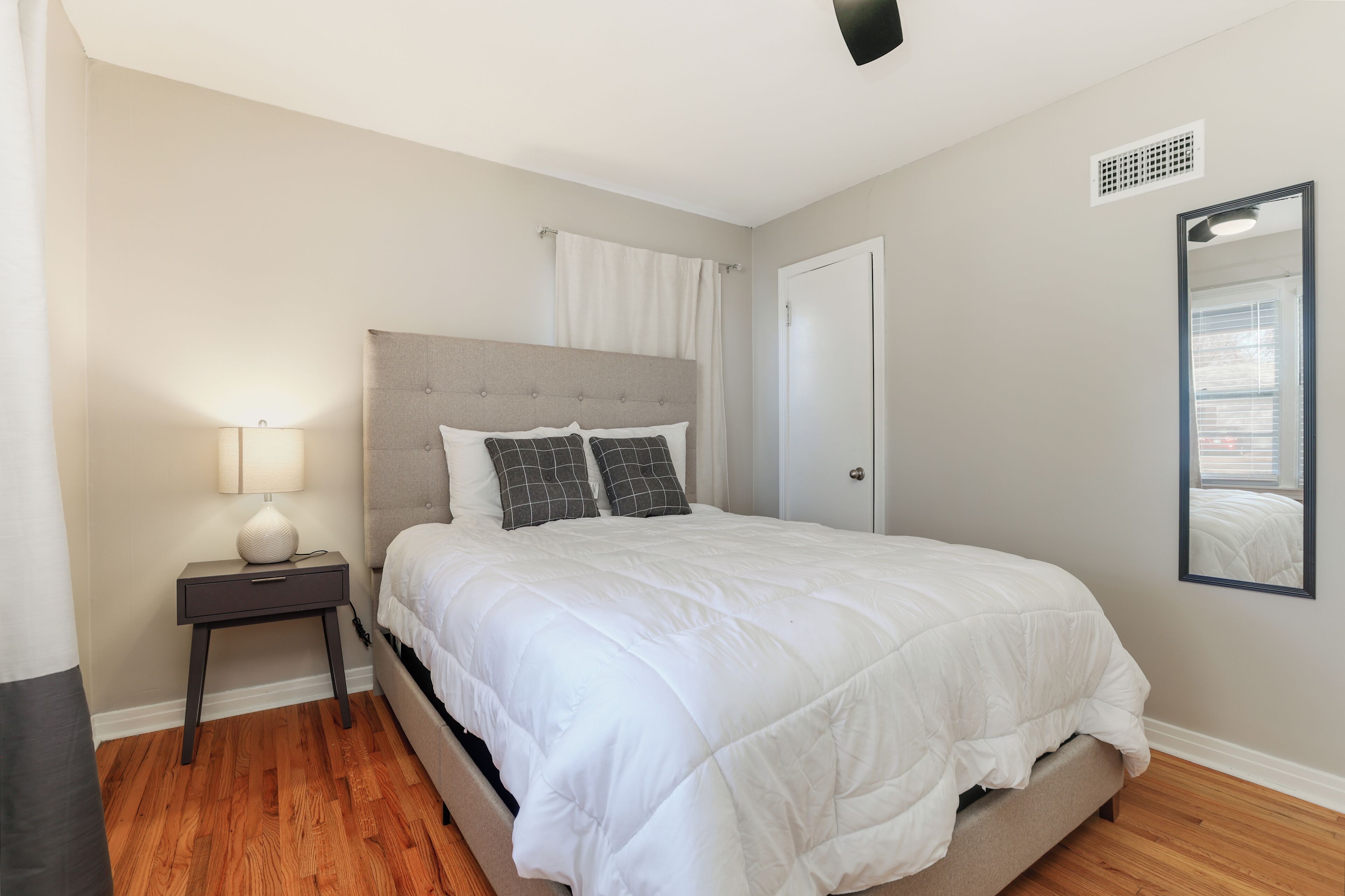 A bedroom with a bed, a nightstand, a lamp, a mirror, and a door.