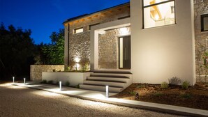 Uma casa moderna com fachada de pedra, entrada bem iluminada e acesso por caminho de cascalho.