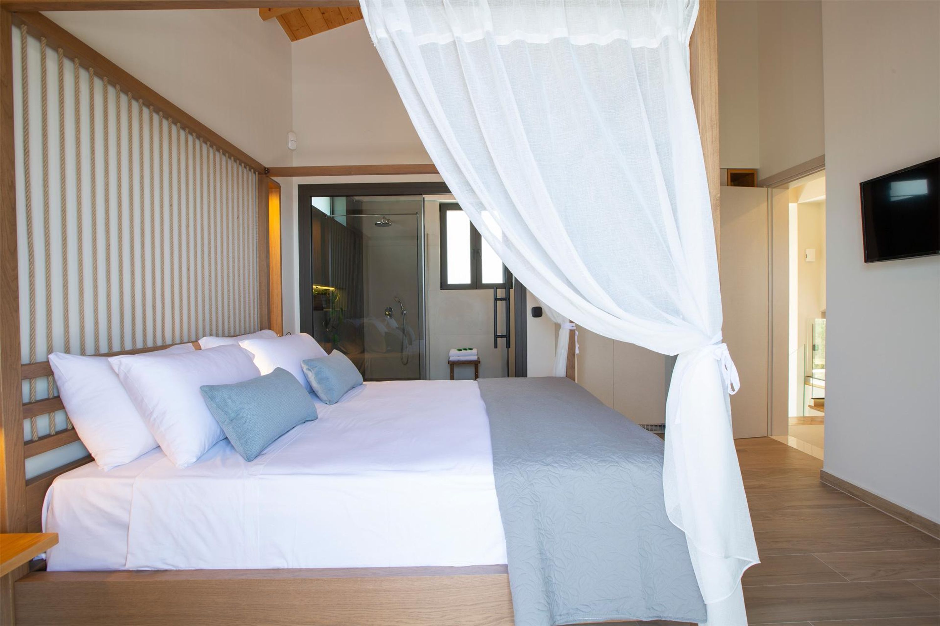 A modern bedroom with a large bed, a television, and a glass shower area.