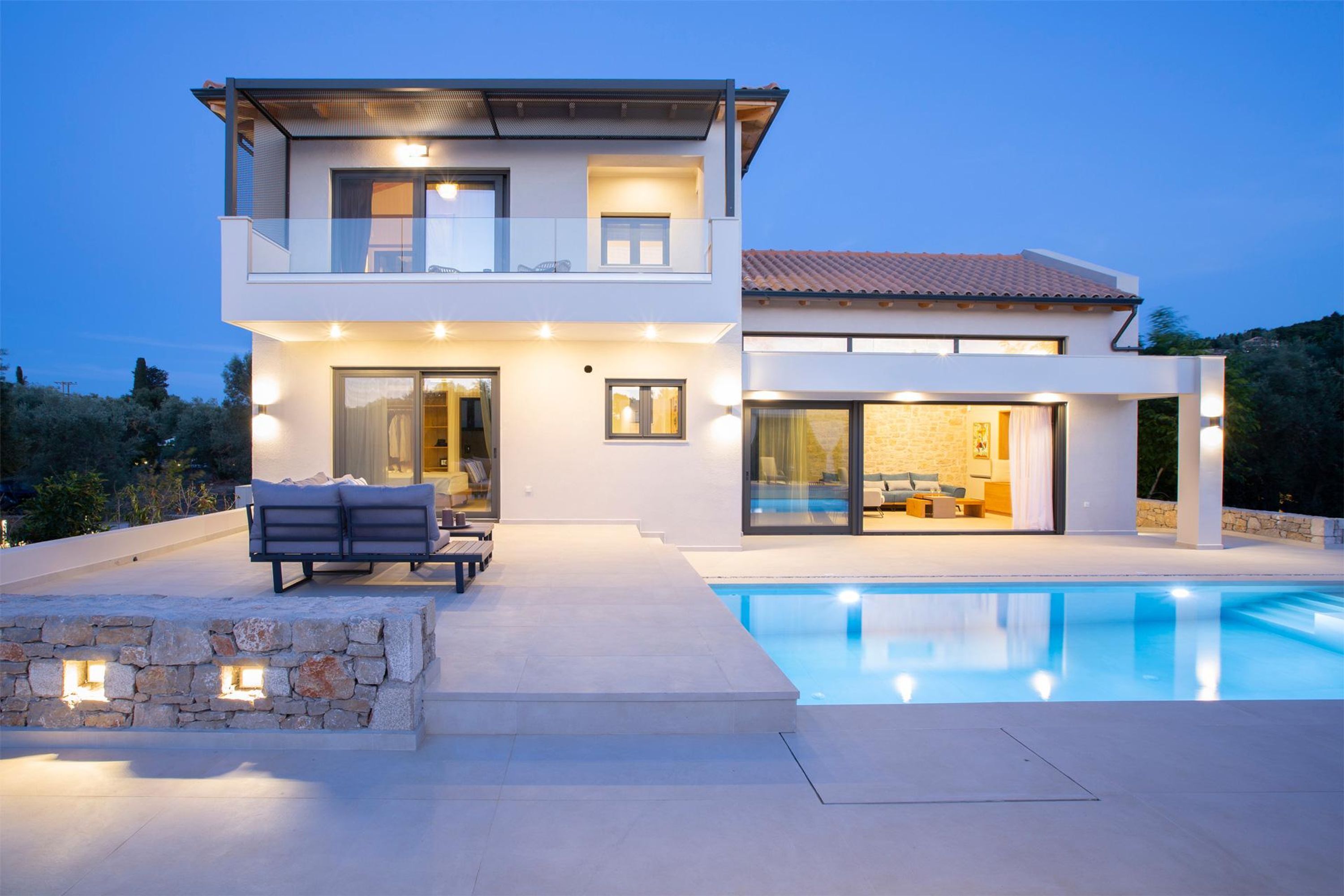 A modern two-story house with a swimming pool, outdoor seating, and a stone wall.