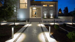 Une maison moderne avec une façade en pierre, une entrée bien éclairée et un chemin menant à la porte.