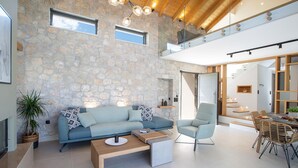 Un salon moderne avec un mur en pierre, un canapé bleu, une table basse en bois et un coin repas avec des chaises en osier.