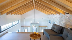 Un loft moderne avec un plafond en pente, des murs en pierre, un grand canapé et une table basse en bois sur laquelle sont posés des verres.
