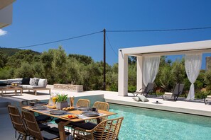 A poolside area with a dining table, chairs, and lounge chairs. - LUXURY  2 BEDROOM VILLA ELIA 4+2 GUESTS (Lefkada)