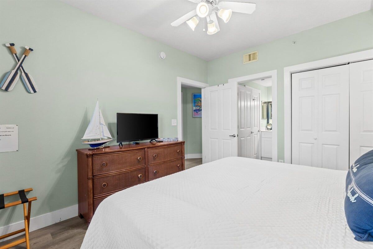 A bedroom with a bed, a dresser, a television, and a ceiling fan.