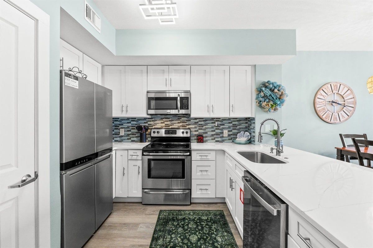A modern kitchen with stainless steel appliances, white cabinetry, and a tiled backsplash.