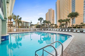 Una piscina con escalera metálica, rodeada de palmeras y edificios modernos.
