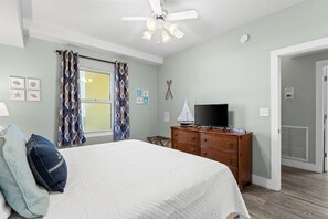 Ein Schlafzimmer mit einem Bett, einem Schminktisch, einem Fernseher und einem Deckenventilator.