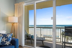 A room with a view of the beach, a sofa with star-patterned pillows, and a lamp. - Celadon 202 | Gulf-Front Views, 2 Pools, Sleeps 8 (Panama City Beach)